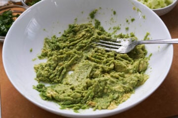 Mashed avocado in a white bowl with a fork.