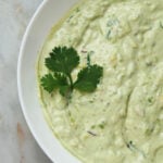 Avocado raita in a white bowl with cilantro leaves garnish.