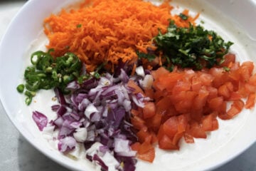 Veggies added to yogurt and spices in a bowl.