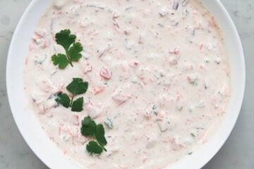 Biryani ratia in a white bowl topped with cilantro leaves.