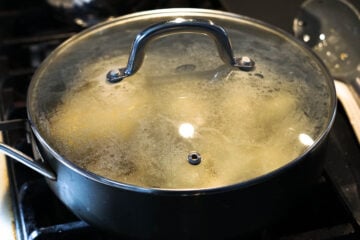 Covered pot cooking potatoes on stove top.