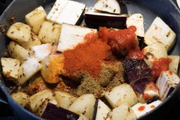 Eggplant and spices added to cooked potatoes in pan.