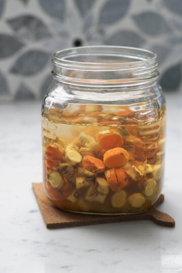 Fresh turmeric root pickle in a glass jar.