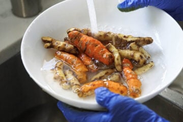 Peeled turmeric roots being rinsed in a bowl.