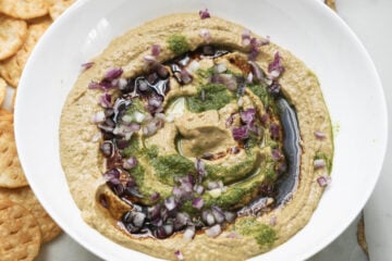Chutneys and red onions added to hummus in a bowl.