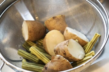 Potatoes and drumstick vegetables in a colander.