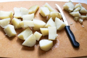 Potato chunks on a cutting board with a knife to the side.
