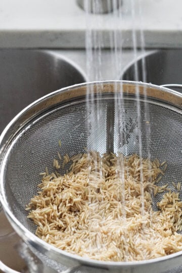 Rinsing brown basmati rice in a colander in the sink.