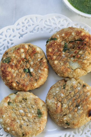 Sabudana vada made in an airfryer on a white laced plate with green chutney to the side.