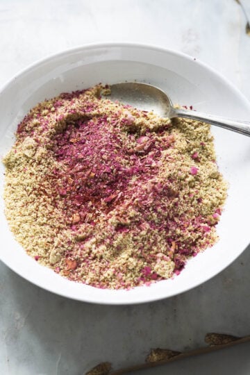 Rose petals and saffron added to thandai powder in a white bowl.