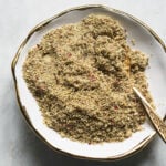 Thandai powder in a small white dish with a gold spoon.