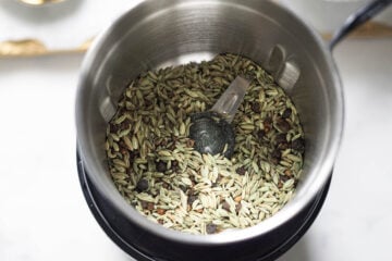 Fennel, black peppercorns, and green cardamom seeds in a spice grinder.