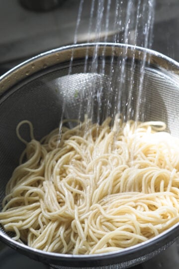 Hakka noodles being rinsed with water.