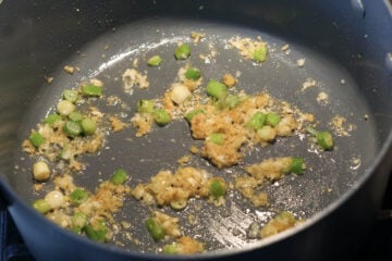 Garlic, ginger, and scallions cooking in oil in a pot.