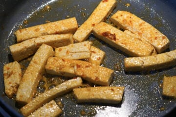 Tofu cooking in oil and sambal olek in a pan.
