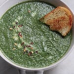 Palak soup in a bowl with red chili flakes and toasted bread.