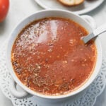 Indian tomato soup in a bowl with toast to the side and a tomato.