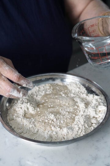 Water added to flour in a bowl to form dough.