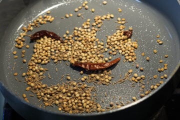 Coriander seeds, cumin seeds, and dry red chilies in a pan.