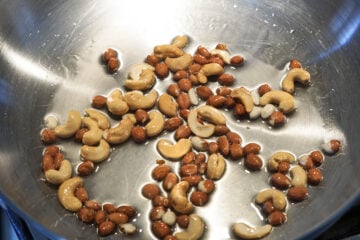 Cashews and peanuts pan frying in a pan.