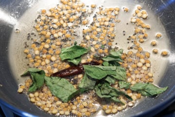 Curry leaves, dry red chilies, chana dal, and urad dal frying in oil.