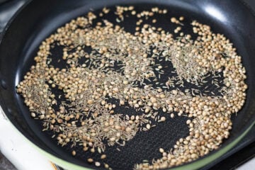 Cumin, coriander, and fennel seeds dry roasting in a pan.