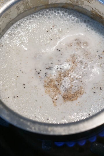 Cardamom milk boiling in a small pan on the stove.
