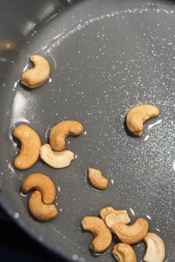 Cashews frying in oil in pan.