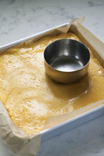 Barfi mixture in a square pan with a ghee greased bowl on top.
