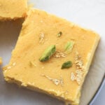 Mango burfi on a plate with pistachios and gold leaf garnish.