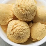 Mango ice cream scoops in a white bowl.