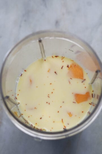 Mango pieces, saffron milk and sugar in a bllender jar.