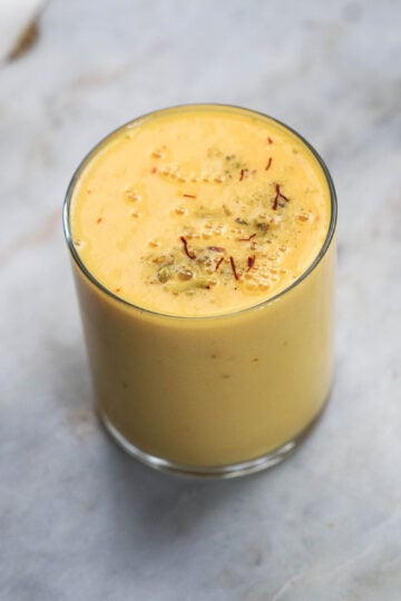 Glass of mango milk with saffron strands on top.