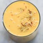 Mango milk in a glass with saffron strands and crushed pistachio.