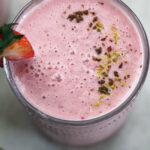 Top view of a glass of strawberry lassi with pistachio crumbles.