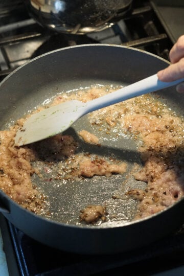 Mixing ginger, garlic, and onion puree with oil and cumin seeds.