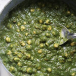 Chana saag in a pot with a silver serving spoon.