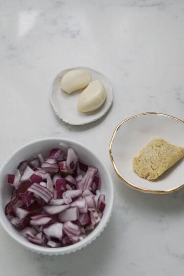 Red onions, two garlic cloves, and an inch of frozen ginger in small plates.