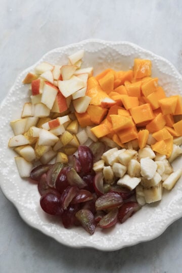 Chopped fresh fruits on a white lace plate.