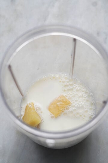 Pineapple pieces in yogurt, milk in a blender jar.