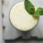 Top view of a glass of pineapple lassi with a sprig of mint leaves.