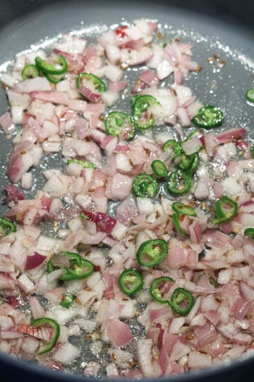 Onions, green chilies, cumin seeds cooking in oil in a pot.