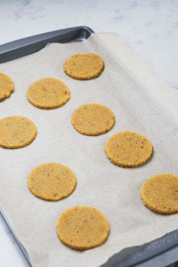Circle cut outs of badam puri on parchment paper on a cookie sheet.