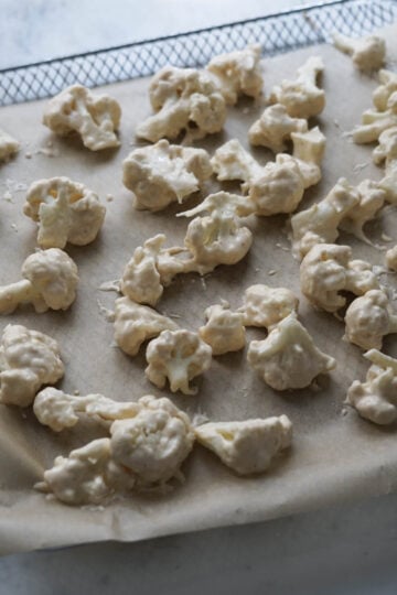 Battered cauliflower florets on a parchment paper lined air fryer tray.