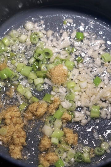 Garlic, ginger, and scallions in oil in a pan.