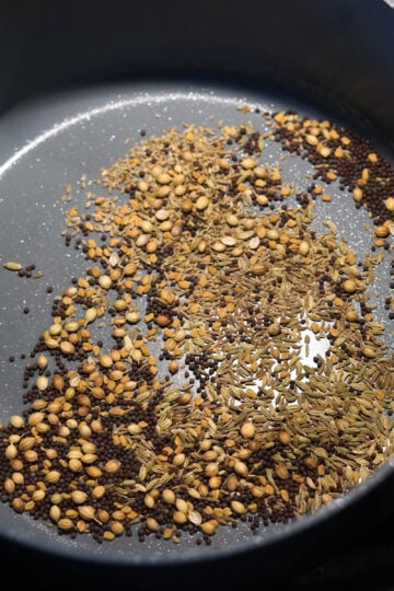 Achari spice blend spices in a pan being roasted.