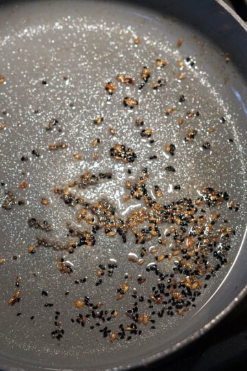 Mustard seeds, kalonji seeds, and cumin seeds in oil in a pan.
