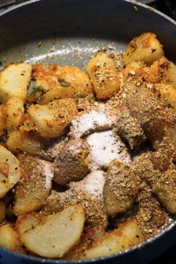 Cubed potatoes, achari spice mix, and salt added to pan.