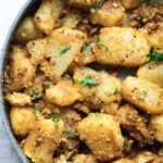 Achari aloo in a pot with cilantro leaves.