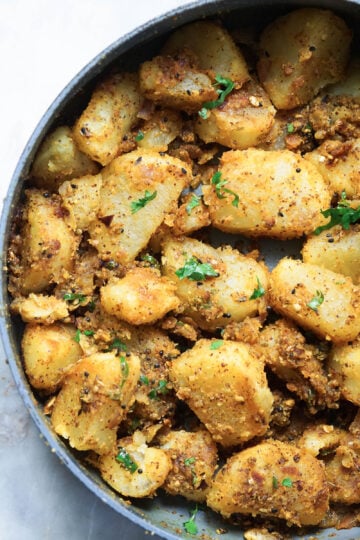 Achari aloo in a pot with cilantro leaves.